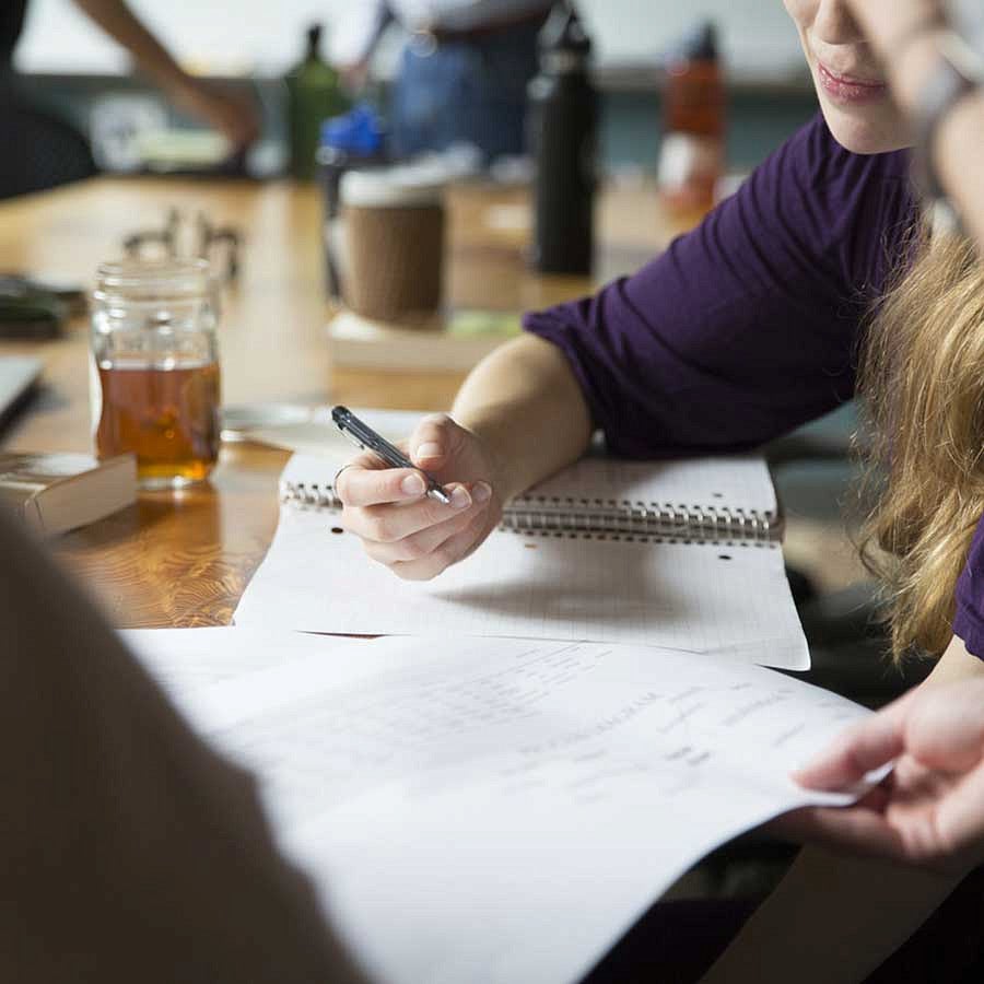 People writing in notebooks while studying at a table People writing in notebooks while studying at a table